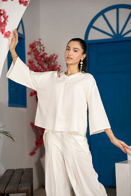 Side profile showing one-shoulder slit detail, relaxed mid-length sleeves and pleated pants