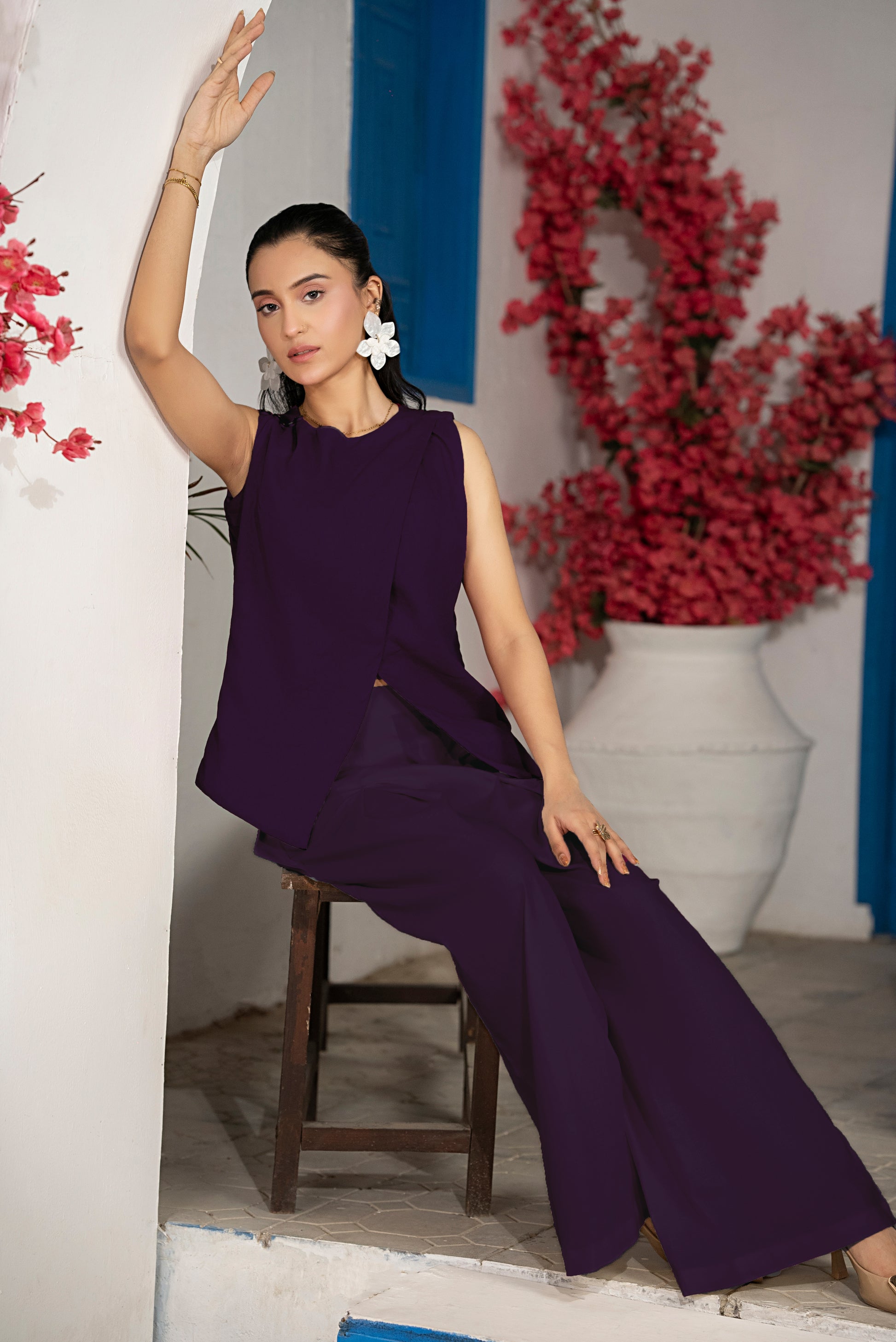Woman in a purple outfit sitting on a stool with floral decorations in the background