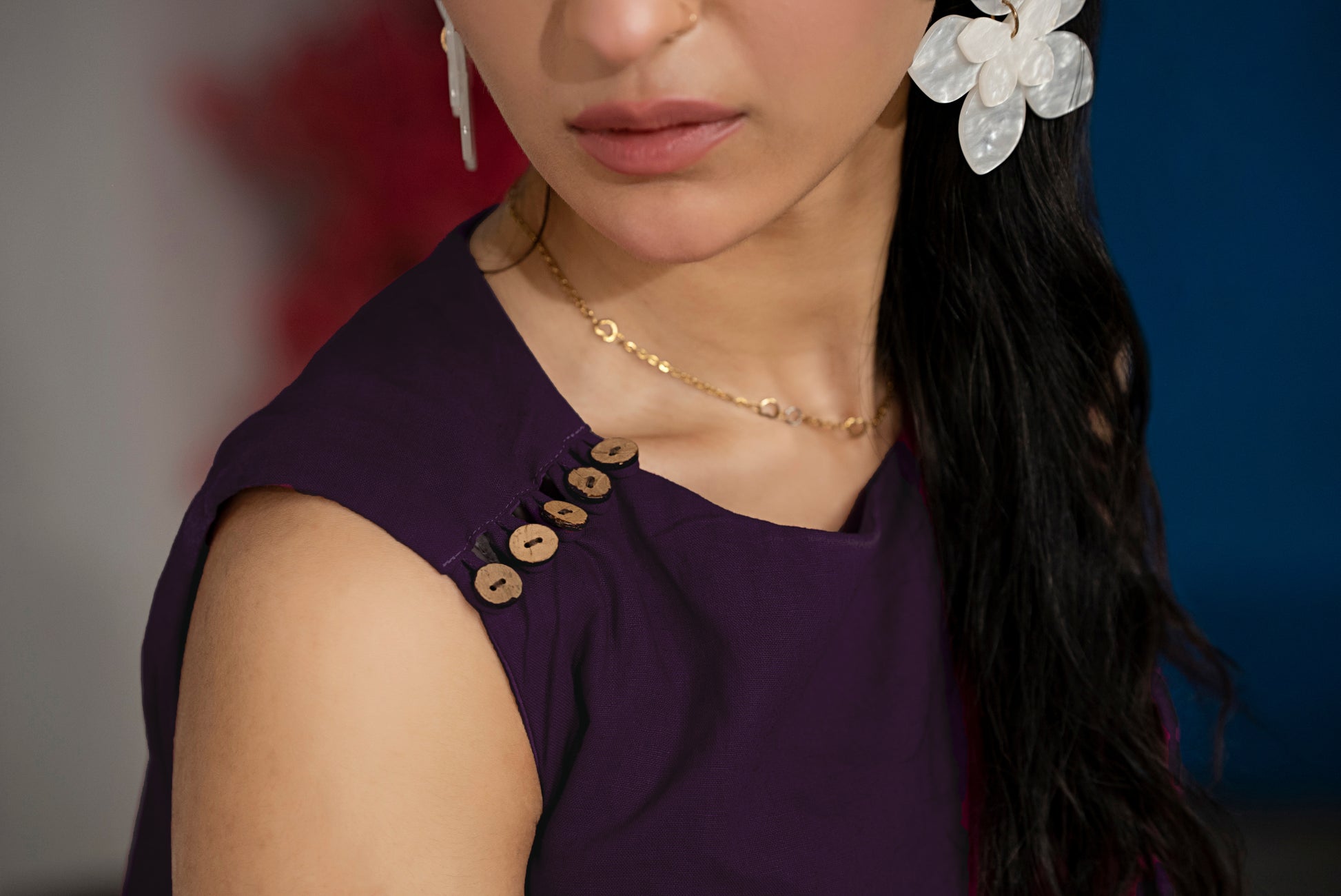 Close-up of a person wearing a purple dress with gold buttons, gold necklace, and white earrings.