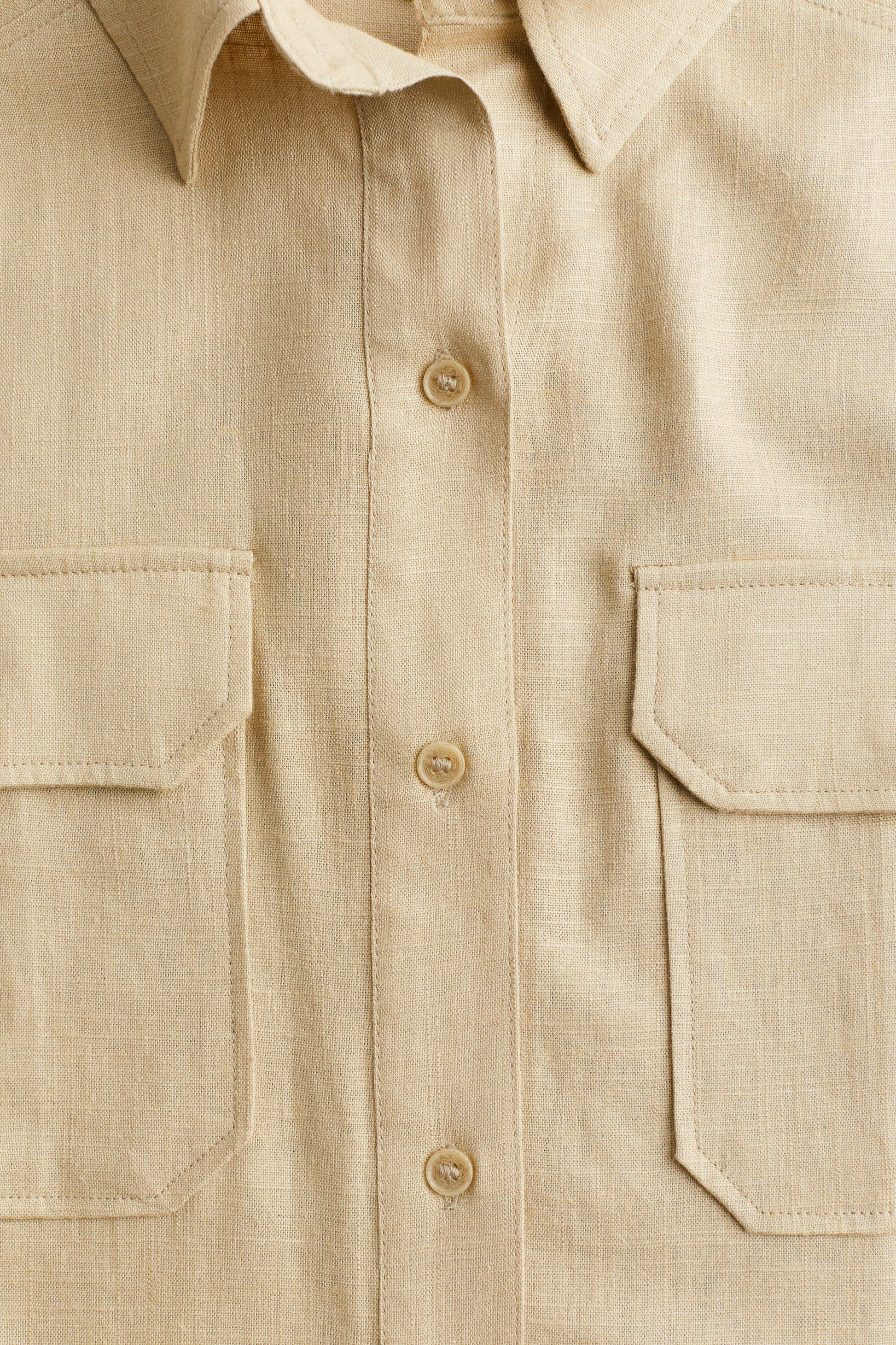 Close-up of a beige button-up shirt with two front pockets.