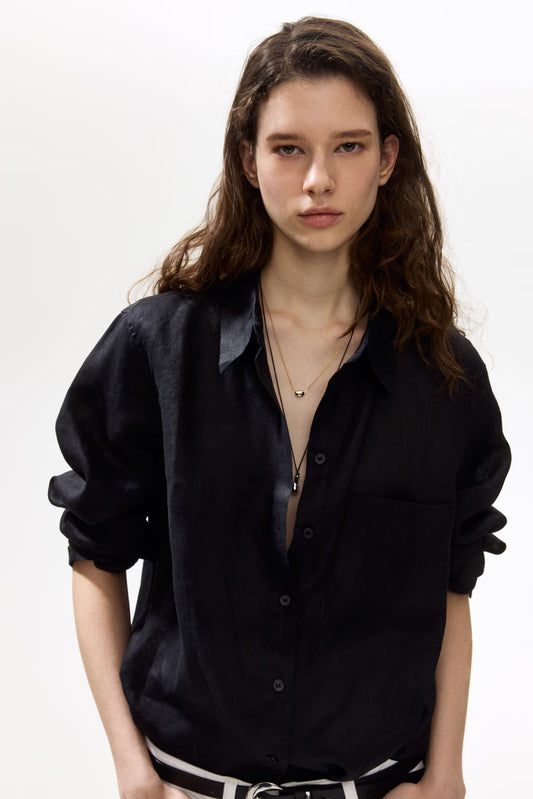 Woman wearing a black linen shirt with a plain background